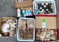 Photo showing four plastic baskets and a box filled with various crafting supplies including many bottles of paint, wooden shapes, metal findings, and wooden clothespins.