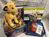 Photo showing Lion King Simba plush sitting on top of two Disney-themed metal tins and the Disney Cruise Line 2010 photo album box in the background.