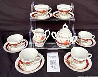 Full view of porcelain tea set with 6 cups, 6 saucers, sugar bowl with lid, and creamer showing floral and autumn leaf pattern.