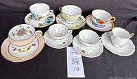 Photo showing six porcelain teacups with matching saucers, each with unique floral or decorative designs and gold trim.