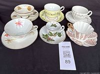 Full set of six porcelain teacups and saucers with varying designs displayed on black cloth.