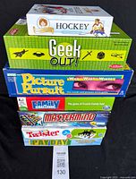 Stack of seven boxed family board games: Hockey, Geek Out!, Picture Pursuit, Family Challenge, Mastermind, Twister, Payday.