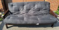 Wooden futon sofa with tufted black cushion, arms and backrest upright
