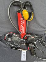 View of all items together: red manual air pump, two electric air pumps, two soldering irons, yellow ear protection headphones