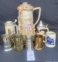 Full display of eight vintage beer steins and tankards showing various materials, designs, and sizes arranged together.