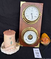 Clock, barometer mounted on wood plaque, small lighthouse figurine, and Bosson Old Salt figurine shown together on black backdrop