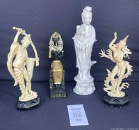 Front view of four figurines: Asian woman porcelain figurine, Egyptian pharaoh, two cream-colored carved fantasy figures on black bases.