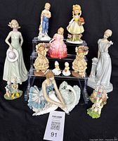 All 11 figurines displayed on black cloth backdrop, showing variety of sizes and styles including women, children, and animals.