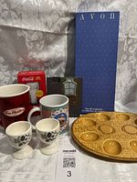 Photo showing the McDonald's Coca-Cola cup in original packaging, Tim Hortons mug, Cherished Teddie mug, 2 beige floral egg holders, Avon utensil holder box, and brown egg dish.