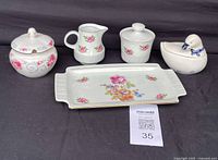 Full set of vintage porcelain items displayed together on black background, showing tray, lidded sugar bowl, creamer, small lidded container, and duck-shaped sugar bowl with floral designs.