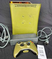Front and side view of Xbox 360 Halo 3 Limited Edition console with controller and power supply cables visible. Olive green/gold plastic with orange accents and Halo 3 branding.
