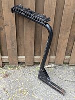 Angle view of black metal bike rack showing vertical support arm and hitch mounting tube with bolt holes.