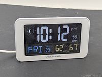 Front view of the AcuRite digital alarm clock showing time as 10:12 PM, date Friday May 23, indoor temperature 62°F and outdoor temperature 67°F.