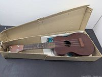 Ukulele inside original cardboard box, showing entire body and neck of the instrument.