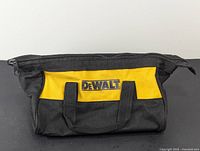 Front view of DeWalt canvas tool bag showing black and yellow colors, DeWalt logo, and carrying handles.