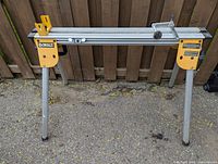 DeWalt yellow and silver compact miter saw stand with four legs set on pavement, showing full front and side view.