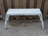 Front view of folding aluminum site bench showing rectangular slatted top and legs spread for support.