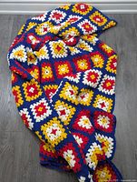 Full view of folded granny square crochet blanket laid on floor, showing red, blue, yellow, and white pattern squares.