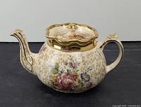 Front angle of the vintage hand painted floral teapot showing the spout, handle and floral designs with gold detailing on lid rim and spout tip.