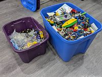 Two large plastic storage bins (blue and purple) filled with mixed LEGO pieces