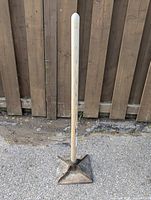 Full view of landscaping ground tamper standing vertically on concrete in front of wooden fence.