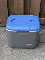 Front view of large Coleman cooler on asphalt with wooden fence background