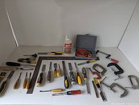 Image showing spread of assorted hand tools including chisels, clamps, wood glue, square, hole saw set and files on white background.