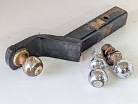 Photo of three trailer hitch balls, one mounted on a hitch receiver mount and two separate balls placed next to it showing signs of rust and wear.