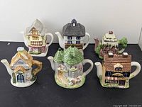 Lot of six ceramic novelty teapots shaped like domiciles including cottages, Victorian pub, and stone castle