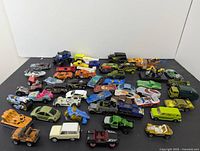 Wide view of the lot showing a variety of miniature die-cast toy cars including trucks, race cars, motorcycles and a helicopter.