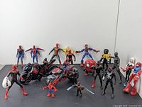 Group photo showing 16 Spider-Man themed action figures and a black Spider-Man motorcycle toy vehicle, arranged on a flat surface against a white background.