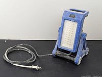 Full view of the blue Mastercraft work light, showing front LED panel and attached power cord coiled beside it.