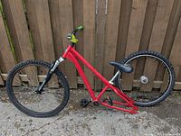 Side view of red Mongoose bicycle frame missing rear wheel tire and chain, shows front suspension fork and front wheel attached.