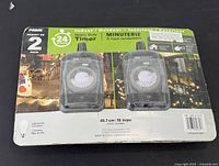 Front of sealed packaging showing two heavy duty timers with a 24-hour dial setting for indoor/outdoor use, suitable for LED and CFL bulbs.