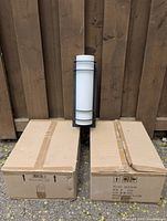 Three modern exterior wall lights with one unboxed and two boxed units, shown against wooden fence.