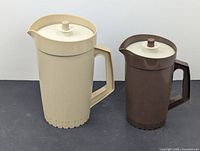 Pair of vintage Tupperware juice pitchers, one beige and one brown, with lids and handles, displayed side by side.
