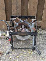 Propane gas burner on metal stand with cross-shaped support frame and attached gas regulator and valve