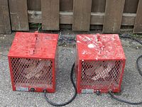 Two red Uniwatt electric site heaters housed in metal cages shown side by side from front angle outdoors.
