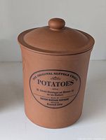 Front view of terracotta potato storage crock with lid on top.