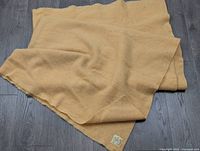 Folded vintage wool blanket laid on dark wood floor, showing size and soft orange color.
