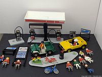 Full set displayed on plain background showing gas station canopy, gas pumps, two vehicles, nine figures, bicycles, signage boards, and accessories.