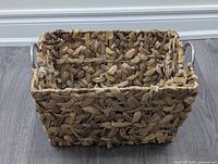 Front view of rectangular basket showing woven water hyacinth texture and round metal handles on sides.