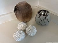 Photo showing the two ceramic vases and three white shell balls arranged on a white surface against a white wall