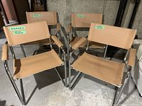 Four vintage kitchen/dining chairs with beige vinyl seats and backs, chrome tubular frames, and armrests clustered together on concrete floor. Visible duct tape repairs under some seats.