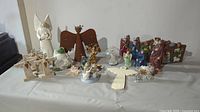 Overall view of various nativity sets and angel figurines including wooden and ceramic pieces, mounted on a table.