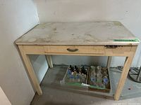 Front view of antique wooden table with metal top and drawer showing dirt and wear.
