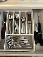 Top down view of assorted cutlery set in a beige plastic tray showing forks, spoons, butter knives, and steak knives with brown handles