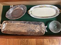 Top view of all four items on green cloth including oval pewter tray, fish plate, long china plate, and glass candle holder.