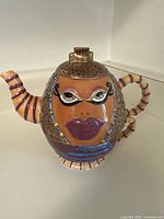 Teapot showing full side view with the stylized face, curly hair details, spout and handle shaped and painted appropriately.