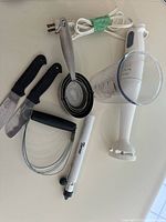 Braun white hand blender/mixer with clear plastic measuring cup and baking utensils on white surface.